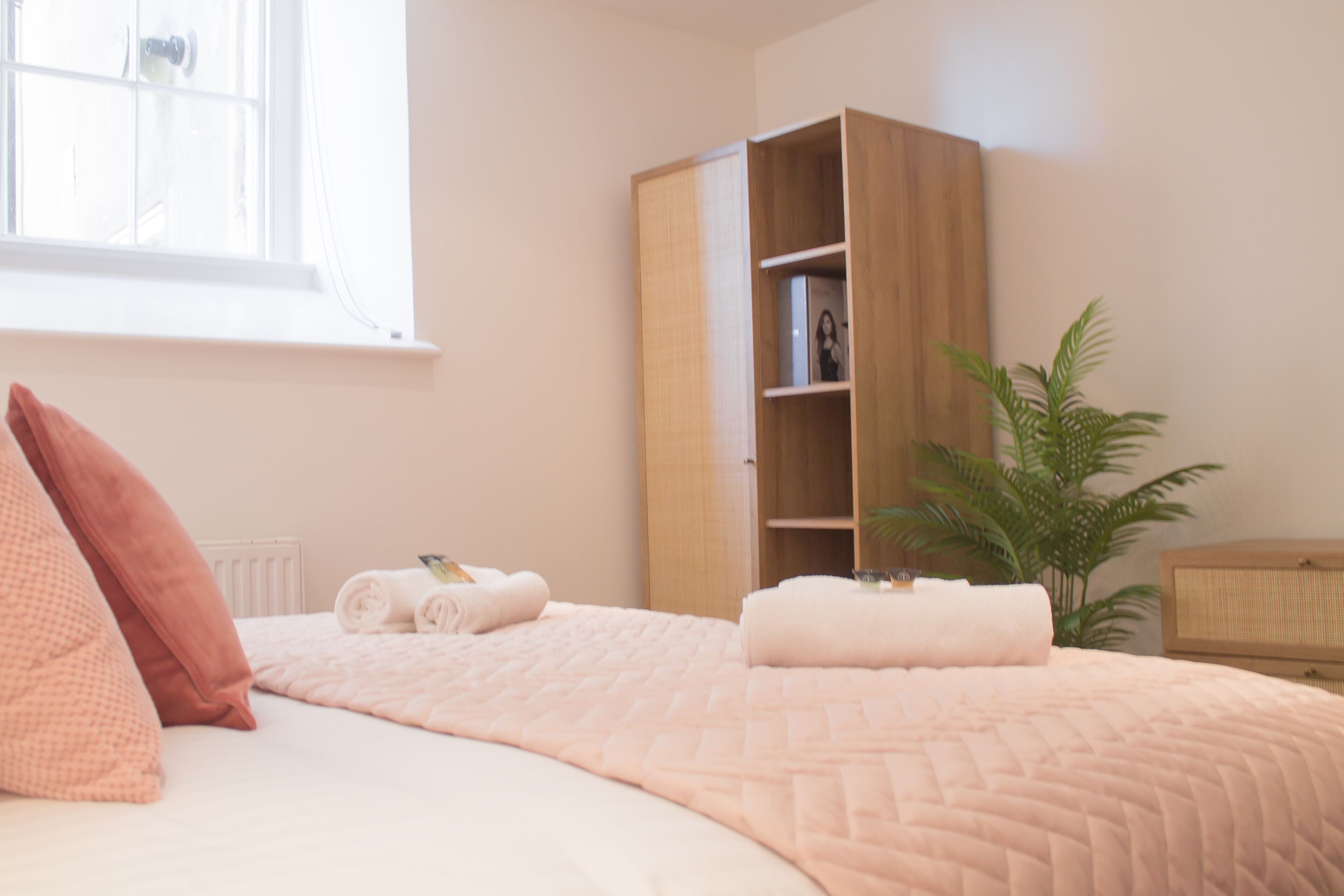 A bedroom with a bed, a wooden wardrobe, a potted plant, and a window.