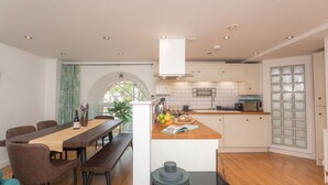 A modern kitchen with white cabinets, a wooden countertop, and a dining area with a table and chairs. - Kensington Chapel Apartments in Bath  (Bath)