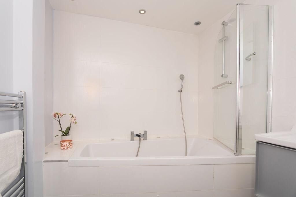 Une salle de bain moderne avec une baignoire blanche, une douche en verre et un petit vase avec des fleurs posé sur le comptoir.