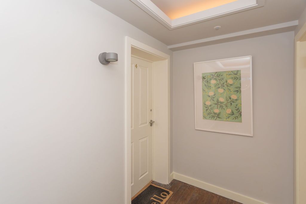 Un couloir avec une porte blanche, une œuvre d’art florale encadrée accrochée au mur et un paillasson sur lequel est écrit le mot « bonjour ».