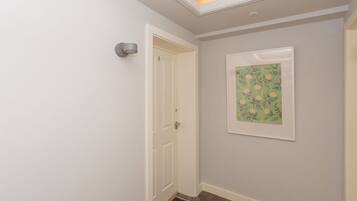 Un couloir avec une porte blanche, une œuvre d’art florale encadrée accrochée au mur et un paillasson sur lequel est écrit le mot « bonjour ».