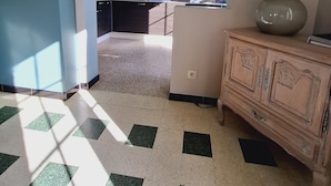 Una habitación con piso a cuadros, viga de techo de madera, televisor montado en la pared y una lámpara sobre un mueble.