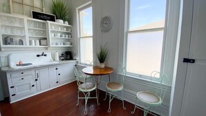 Une cuisine avec des meubles blancs, un plan de travail en bois et une table ronde entourée de chaises. Il y a une horloge au mur et une fenêtre donnant sur la plage.
