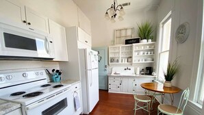Une cuisine dotée de meubles blancs, d’une cuisinière, d’un réfrigérateur et d’un coin repas avec une table et des chaises.