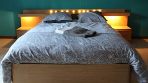 A neatly made bed with a patterned bedspread, two pillows, and a blanket. There are two bedside tables with lamps. - Le Relais du Cheval Blanc (Tenneville)