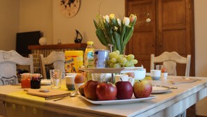 A dining table with a plate of apples, a vase of flowers, and various kitchen items. - Le Relais du Cheval Blanc (Tenneville)
