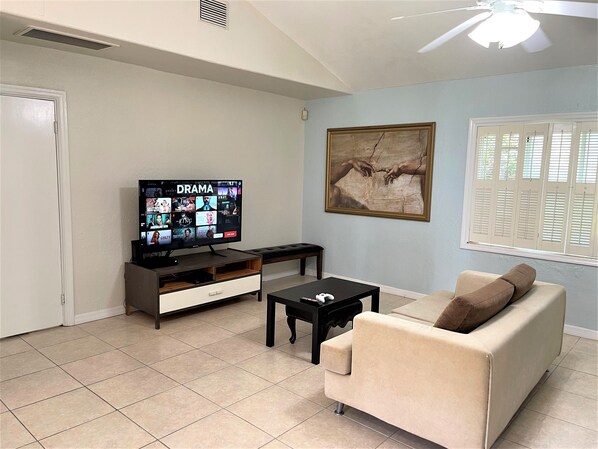 A living room with a television displaying a streaming service interface, a sofa, a coffee table, and a painting on the wall. - Winter Park Oasis (Winter Park)