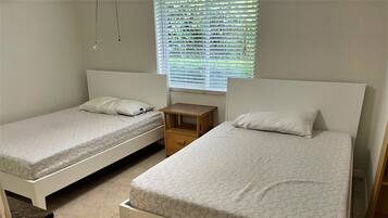 A room with two single beds, each with a pillow and a wooden nightstand.