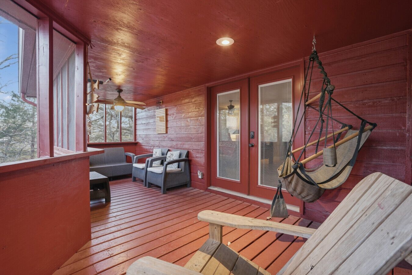Une véranda couverte avec un plancher en bois, un hamac suspendu et deux fauteuils en osier avec des coussins.