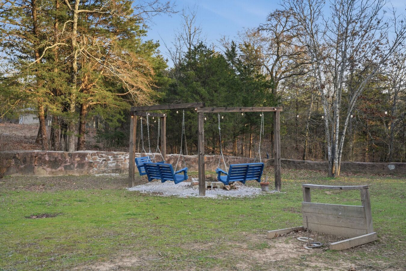 Ein Holz-Schaukelgerüst mit zwei Schaukeln in einer grünen Wiese, im Hintergrund Bäume.
