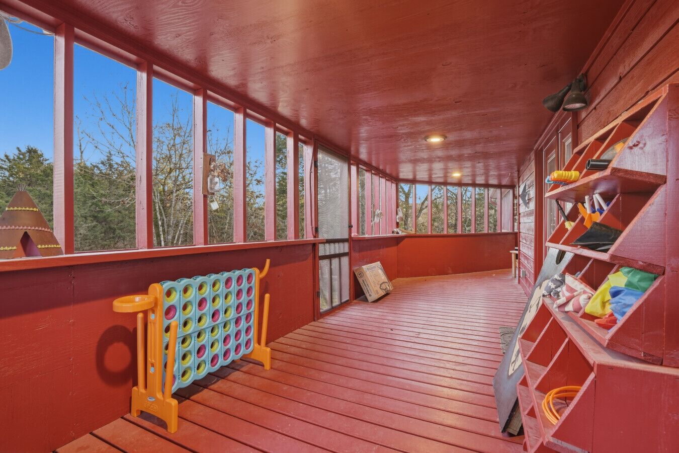 A covered wooden deck with a view of trees, a children's play area, and storage shelves.