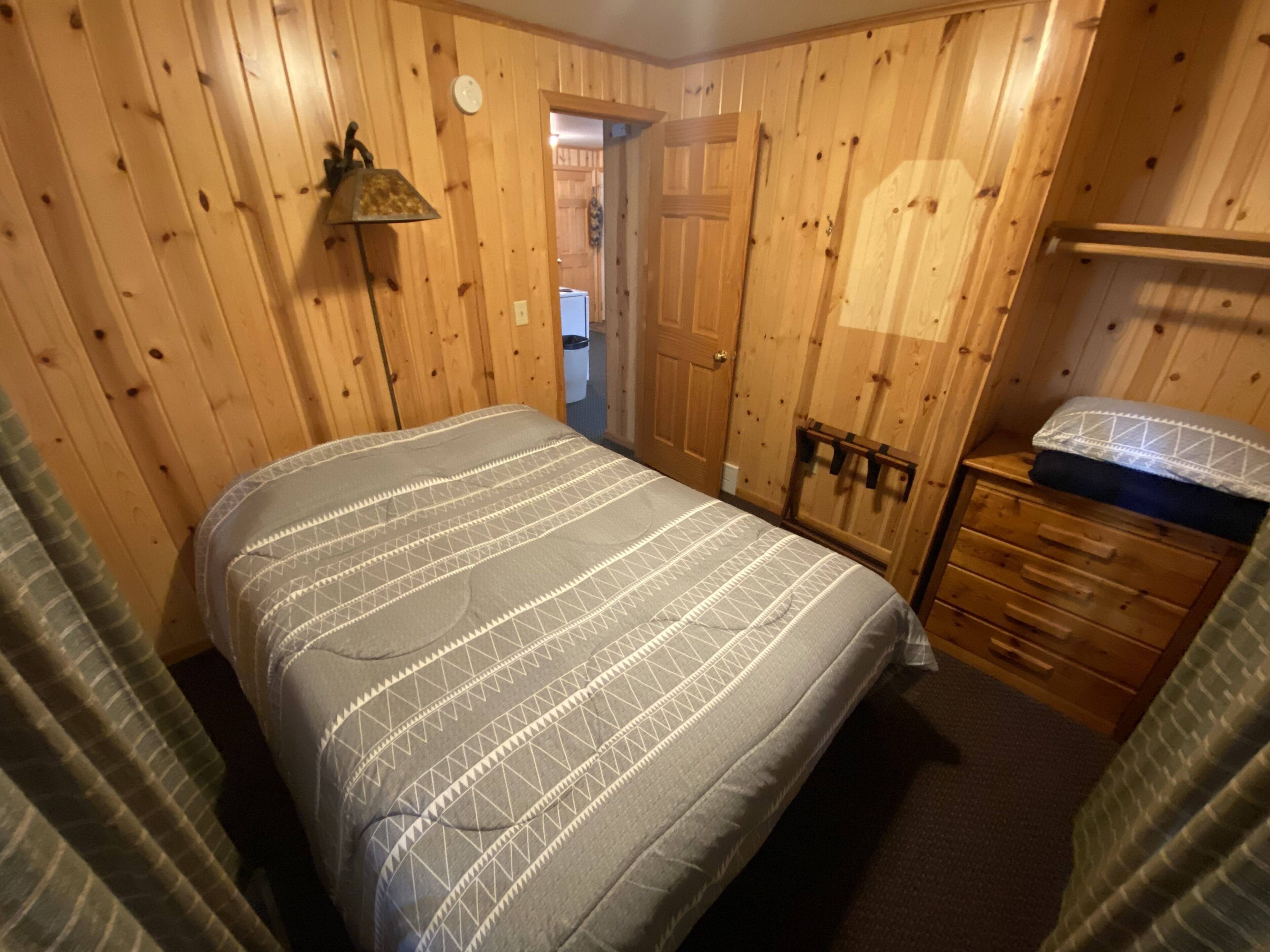 A wooden-paneled bedroom with a bed, dresser, and lamp.
