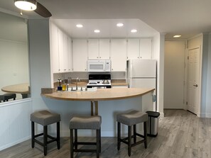 Una cocina moderna con armarios blancos, una isla central con taburetes, un microondas, una estufa y un refrigerador.