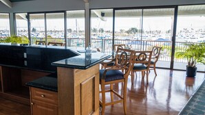 Uma área de bar com balcão de madeira, banquetas e amplas janelas com vista para uma marina.