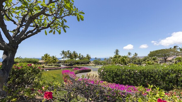 A landscaped garden with a variety of plants and flowers, a tree, and a view of the ocean.