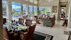Ein großzügiger Wohnbereich mit Esstisch, Stühlen und einer Couch. Große Fenster bieten Blick ins Freie.