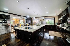 A modern kitchen with a large island, dark wood flooring, and built-in appliances.