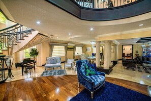 A spacious living area with a grand staircase, a piano, and a plush blue armchair.