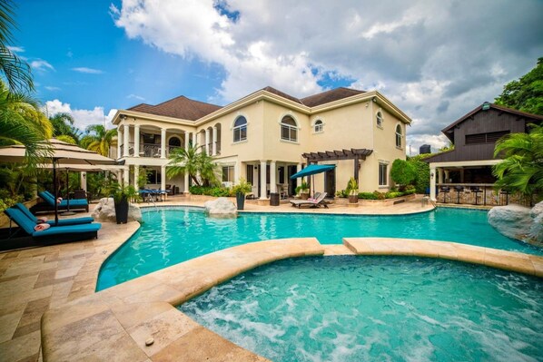A large house with a swimming pool, outdoor seating, and a covered patio area.