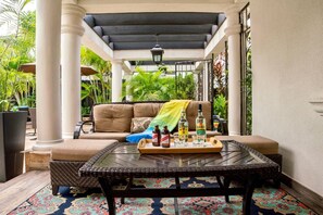 A covered outdoor seating area with a sofa and a table set with bottles and glasses.