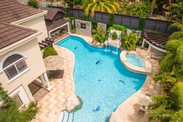 A swimming pool with a curved design, surrounded by a stone deck and palm trees.