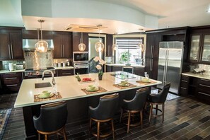 A modern kitchen with a central island, dark cabinetry, stainless steel appliances, and pendant lighting. - Orchids & Palms Villa, Chef, Pool-Montego Bay! (Montego Bay)