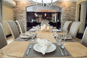 A dining area with a long table set for six, flanked by stone walls and modern kitchen appliances in the background.