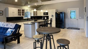 Una cocina amplia con armarios blancos, un refrigerador negro y un comedor con mesa y sillas de madera.