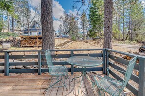 A wooden deck with metal chairs and a table, surrounded by trees and a house in the background. - A-Frame Cabin w/ EV Charger, Arcade & Vinyl Lounge (Pioneer)