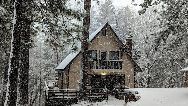 Eine zweistöckige Holzhütte mit einem Balkon, umgeben von schneebedeckten Bäumen.