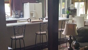 Una cocina equipada con refrigerador, estufa y taburetes de bar. Hay un comedor con mesa y sillas.