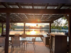 A covered outdoor seating area with a view of a lake and sunset.