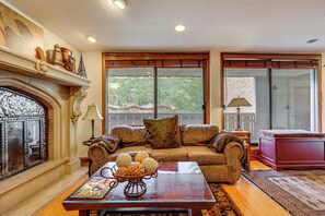 A living room with a fireplace, a sofa, a coffee table with decorative items, and a view through large windows.
