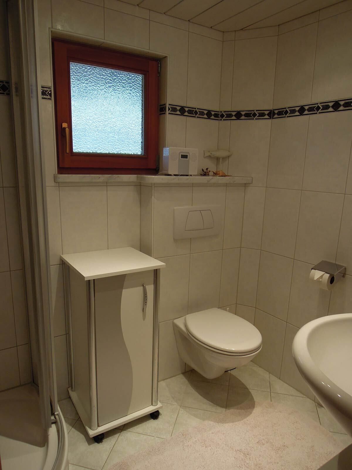 Een kleine badkamer met toilet, wastafel, kast en raam.