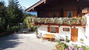 A wooden chalet with a balcony, a bench, and a small garden area.