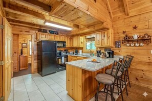 A wooden cabin interior with a kitchen featuring a refrigerator, stove, and bar seating.