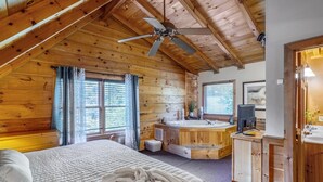 A cabin-style bedroom with a large bed, a ceiling fan, and a hot tub in the corner. - Pigeon Forge | Hot Tub & Arcade (Pigeon Forge)
