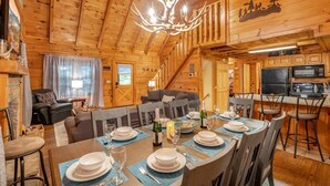 A wooden cabin interior with a dining area set for a meal, a kitchen, and a living room with a fireplace. - Pigeon Forge | Hot Tub & Arcade (Pigeon Forge)