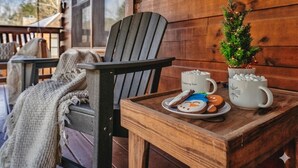 A wooden deck with a chair, a small table with a tray, a Christmas tree, and mugs. - Pigeon Forge | Hot Tub & Arcade (Pigeon Forge)