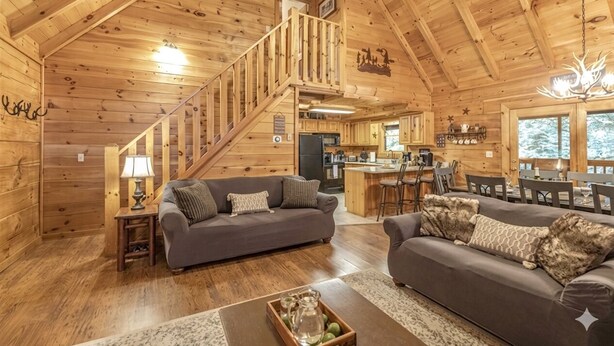 A log cabin interior with a staircase, two sofas, a coffee table, and a kitchen area. - Pigeon Forge | Hot Tub & Arcade (Pigeon Forge)