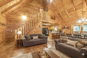 A log cabin interior with a staircase, two sofas, a coffee table, and a kitchen area. - Pigeon Forge | Hot Tub & Arcade (Pigeon Forge)