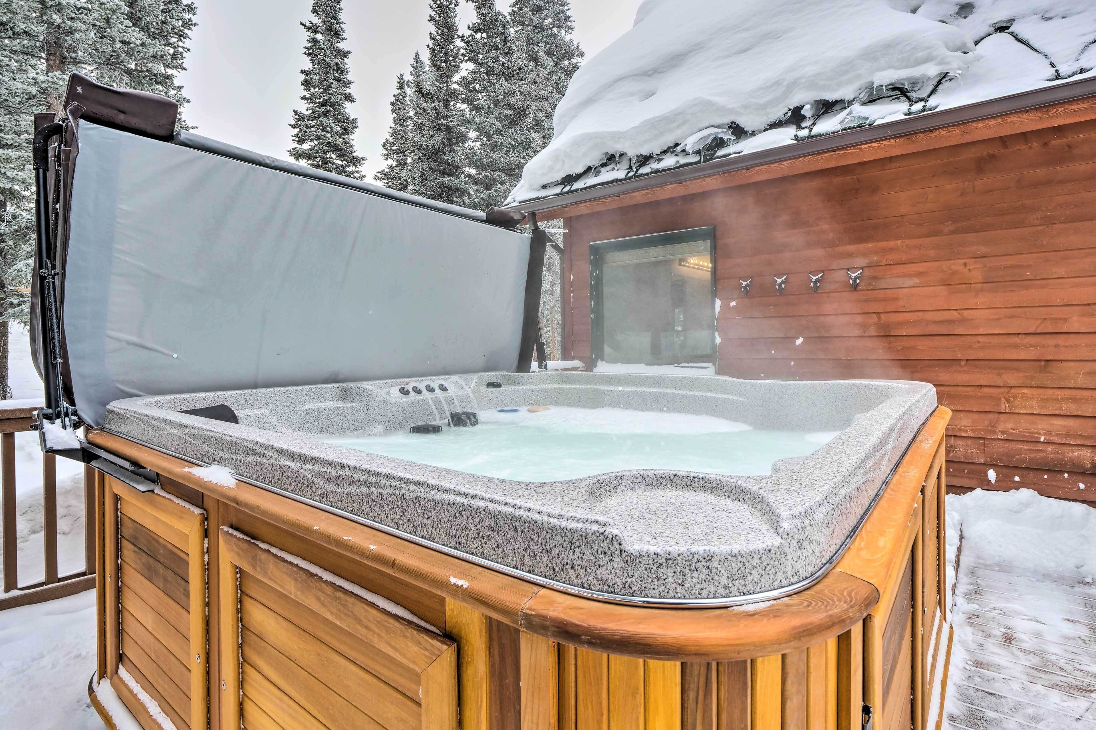 Un bain à remous doté d’une terrasse en bois et d’un espace abrité, entouré de neige et d’arbres.
