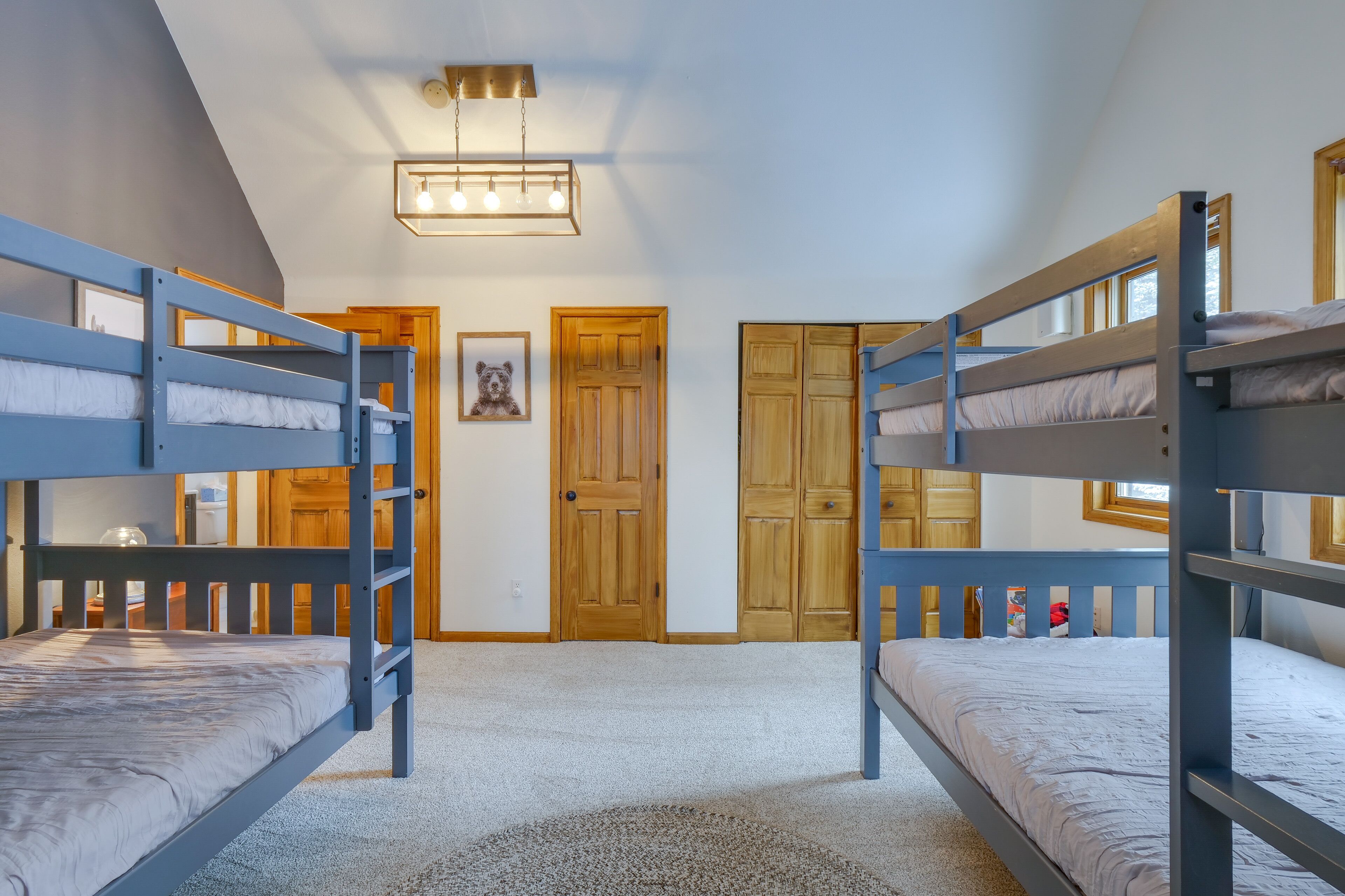 Een kamer met stapelbedden, houten deuren, een lijst met een afbeelding en een plafondlamp.