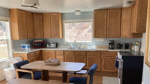 Una cocina con armarios de madera, una mesa de comedor con sillas, un microondas, un tostador y un refrigerador.