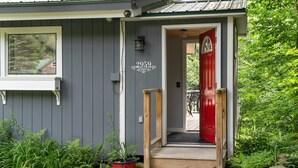 Ein Haus mit roter Tür, der Aufschrift '2959' über der Tür und einer kleinen Veranda mit Stufen zum Eingang.