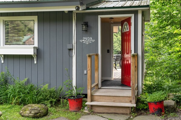 Una casa con puerta roja, el número '2959' sobre la puerta y un pequeño porche con escalones que llevan a la entrada.