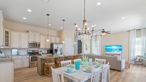 A modern kitchen with white cabinets, stainless steel appliances, and a central island with bar stools. - Heated Pool + Games | Golf Cart | Near Beach (Jacksonville Beach)