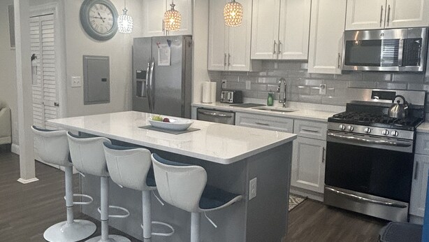 A modern kitchen with white cabinets, a stainless steel stove, a microwave, and a large island with bar stools.