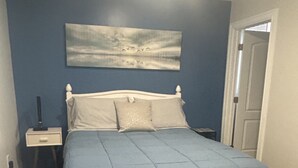 A bedroom with a bed, a bench, a nightstand, and a painting on the wall.