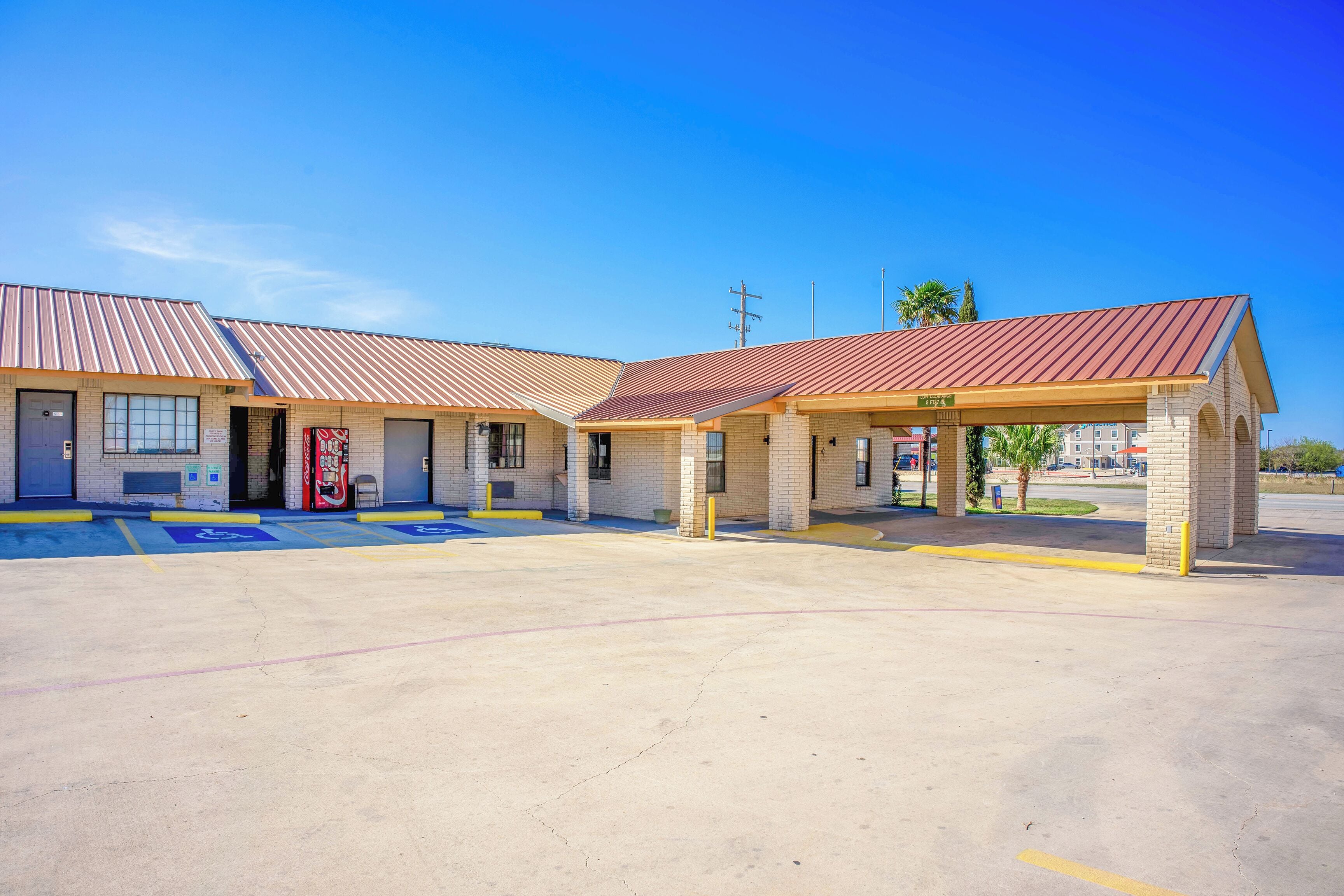 A motel with a central parking area, multiple rooms with brick facades, and a covered outdoor seating area.